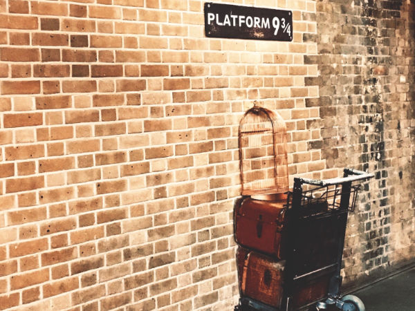 Ein Gepäckwagen steckt in einer Wand über dem die Bezeichnung Gleis 9 3/4 hängt (Szene aus Harry Potter)