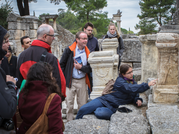 Gruppenaufnahme während einer Exkursion. Eine Person beschreibt eine Inschrift auf einem Grabstein.