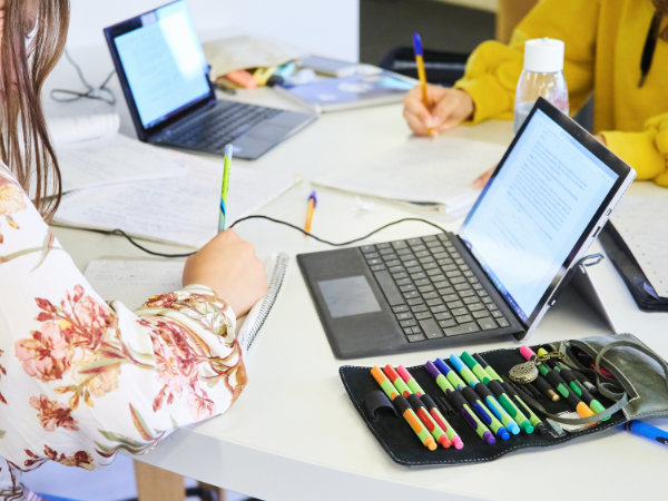 Studentinnen schreiben. Im Hintergrund sind Laptops zu sehen.