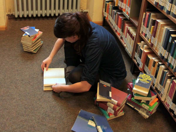 Studentin sitzt in Bibliothek auf dem Boden und liest Literatur